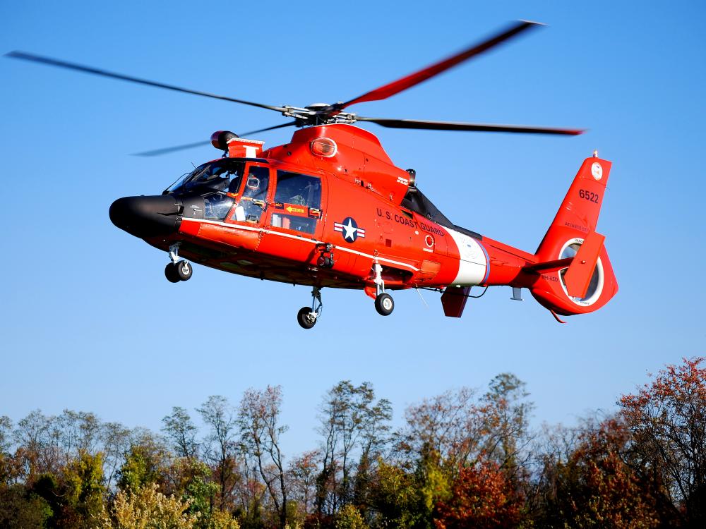 Side view of red helicopter with four blade propellor flying in the air.