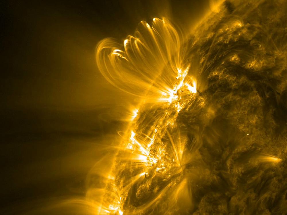 A partial view of the sun focusing on the eruption of a solar flare in bright yellow. The solar flare expands beyond the layer of the sun photographed.