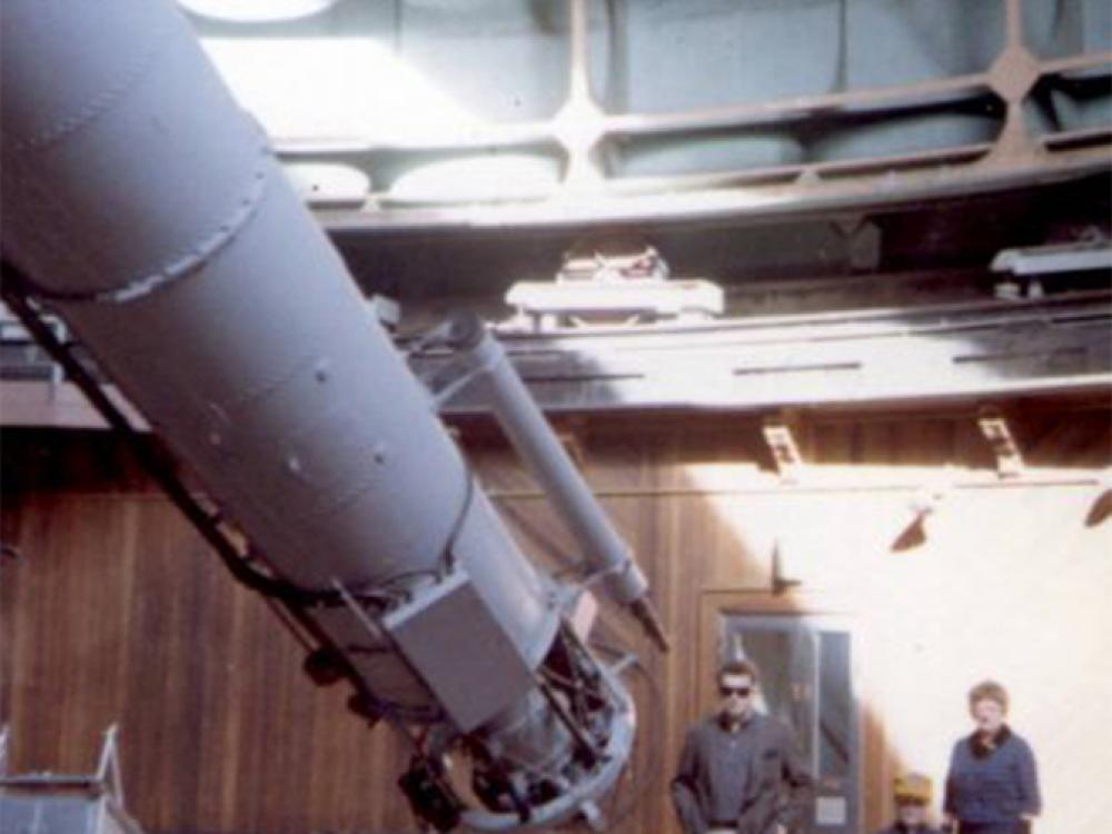 Three people pose near the bottom end of a cylinder-shaped object inside an observatory dome.