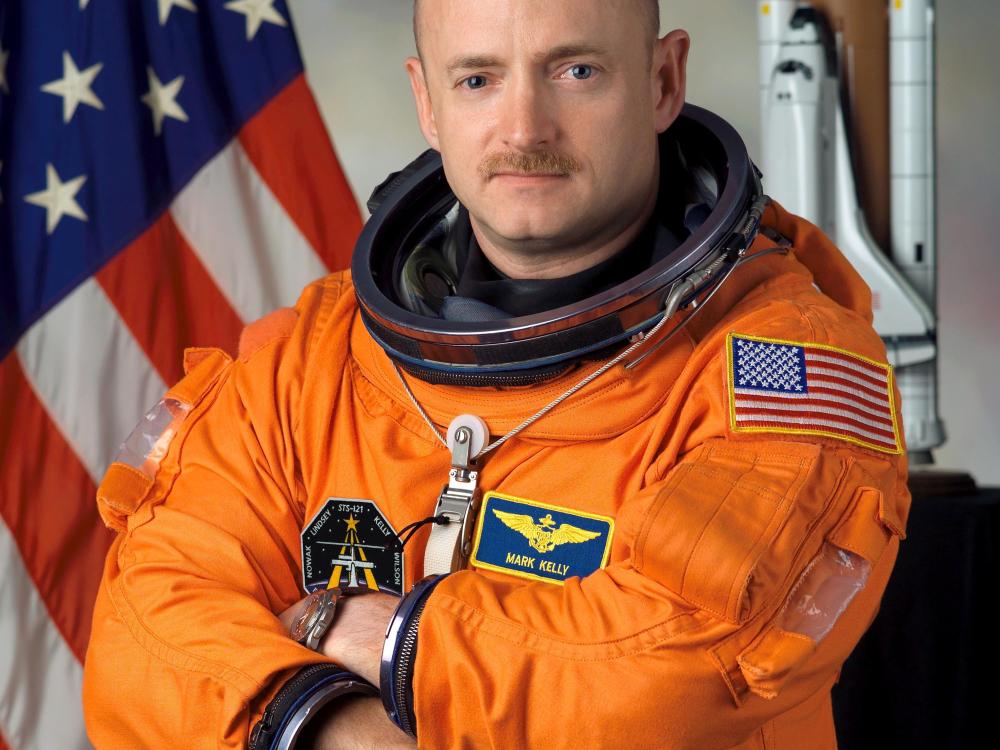 Mark Kelly poses in an orange pressurized astronaut suit for an official photo.