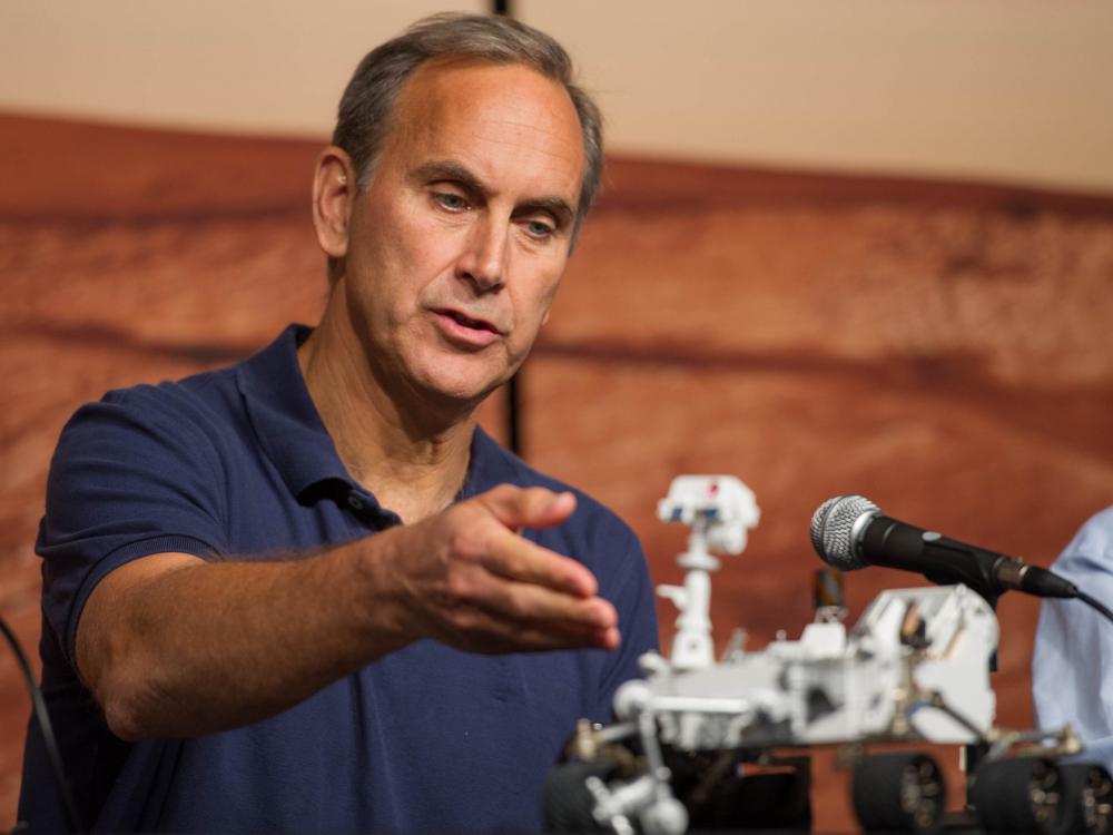 A white man directs his hand towards a Rover model.