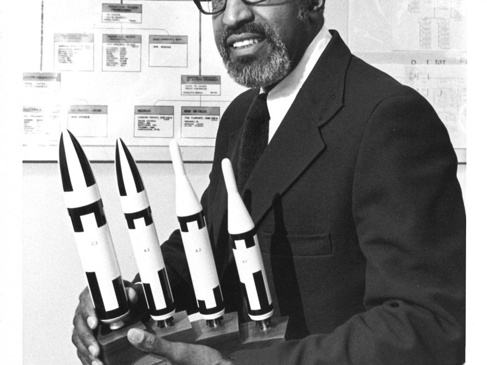 Frank Crossley, an African-American man, sits with a set of trophies featuring rocket figurines.