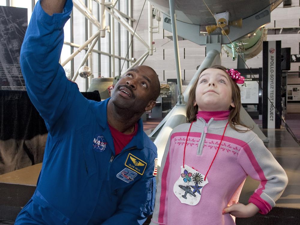 Former Astronaut Leland Melvin, an African-American man, kneels next to a young child at the Museum.