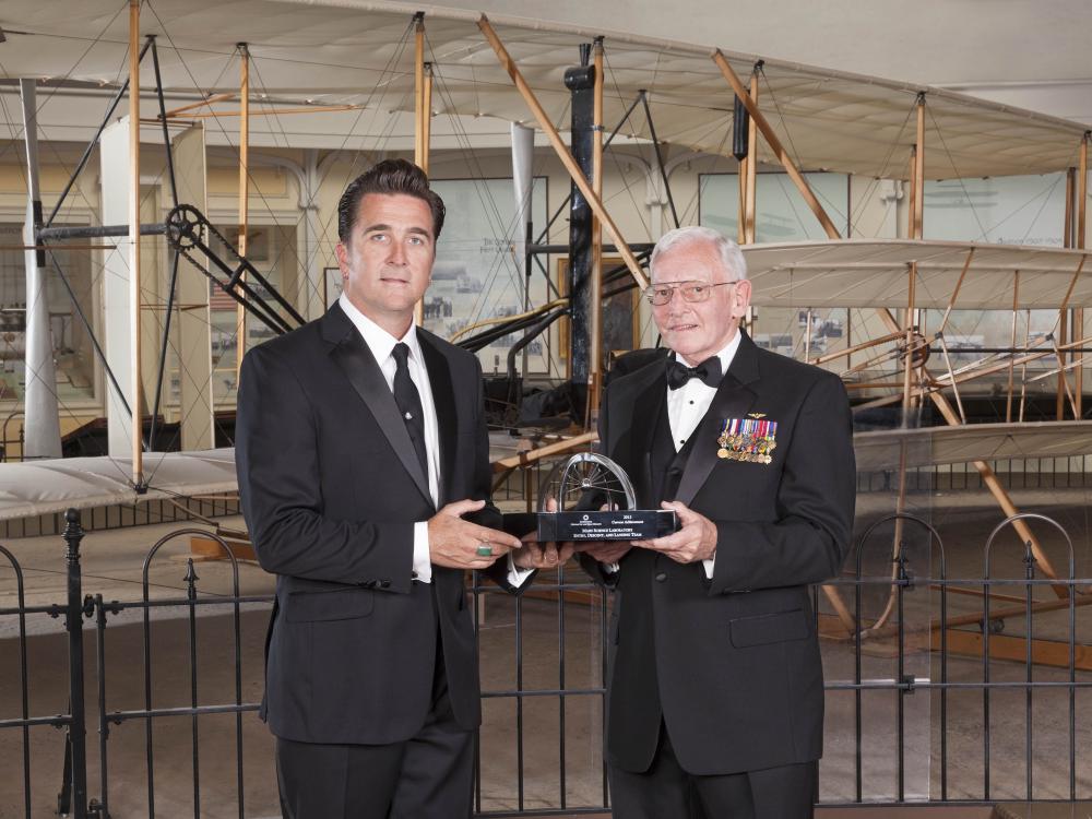 Dr. Adam Steltzner and Gen. Jack Dailey, two white men, pose for a photo as Steltzner accepts a trophy.