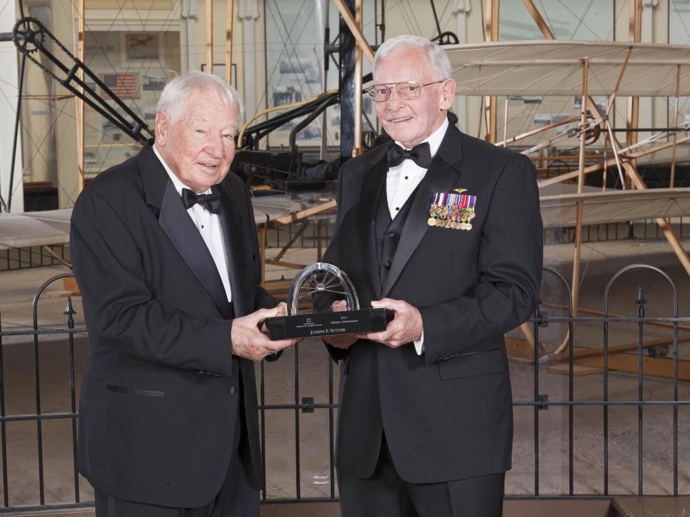 Joseph Sutter and General Jack Dailey, two white men, stand together for a picture while holding a trophy presented to Sutter.