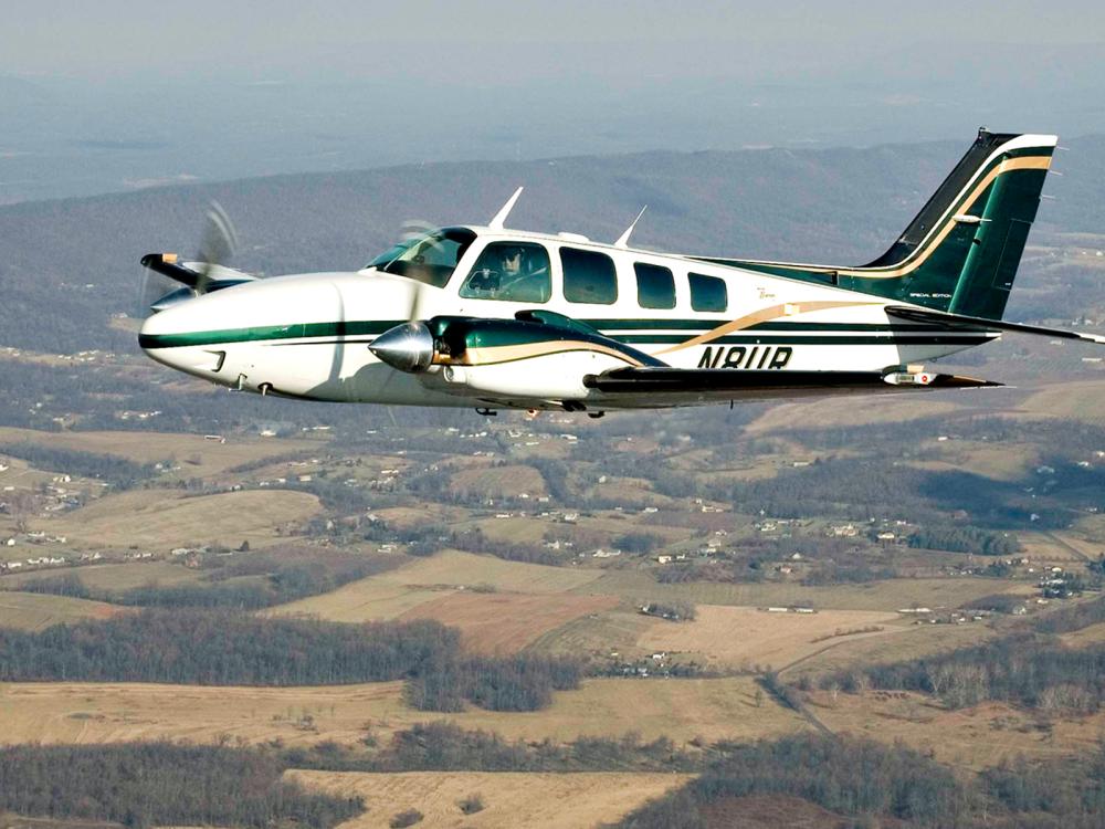 Side view of a white and green monoplane with twin engines in flight. The registration number "N8UR" is painted in a dark color near the rear of the fuselage.