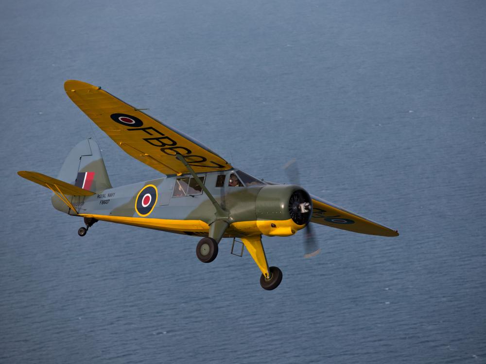 Side view of yellow, olive drab green, and gray monoplane in flight with one engine and fixed landing gear.