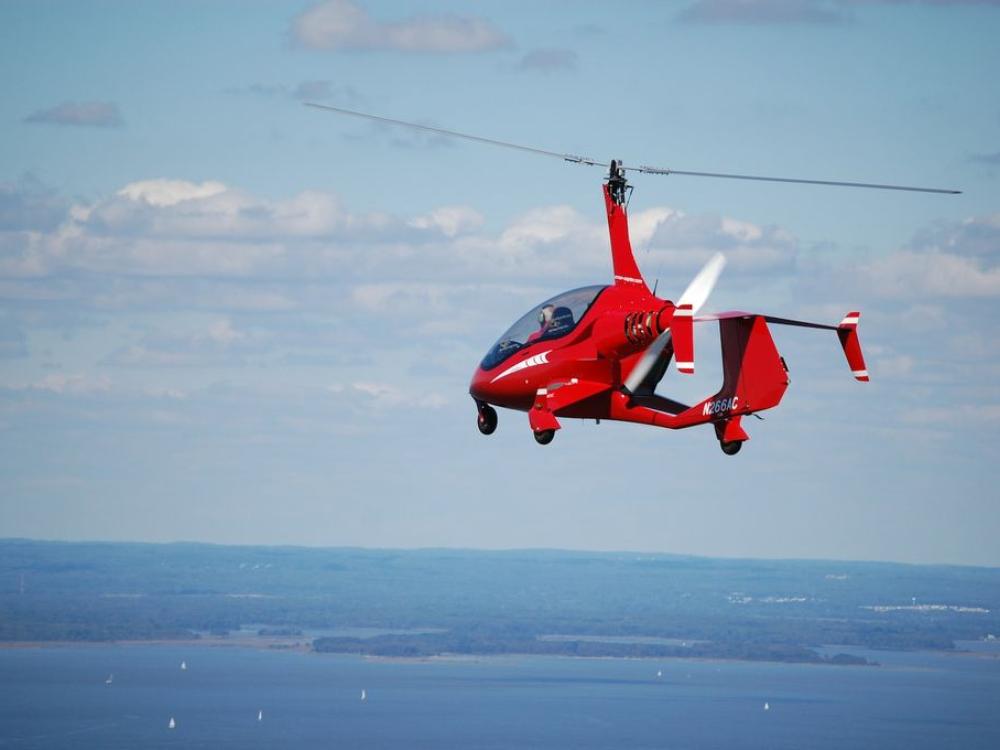 Side view of a small red helicopter in flight with one two-blade propellor above the cockpit.