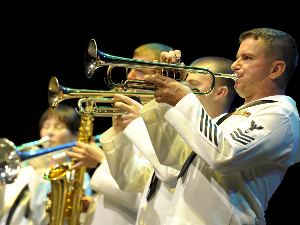 A group of performers in U.S. Navy uniforms play various instruments.