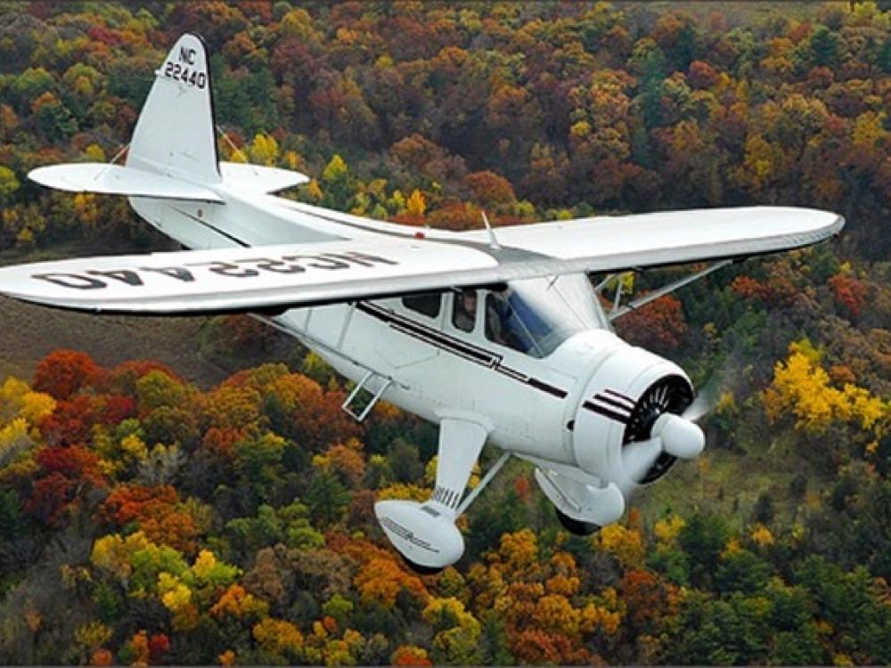 Diagonal front view of a white monoplane in flight with fixed landing gear and one engine.