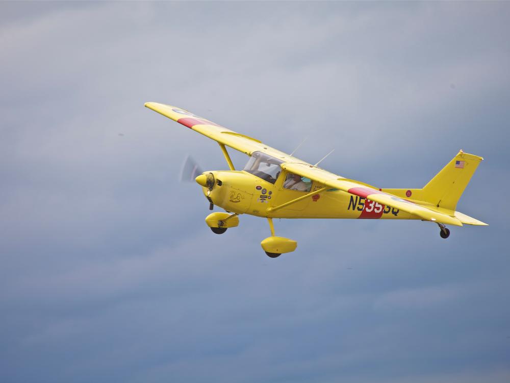 Side view of yellow monoplane in flight with single engine and fixed landing gear.