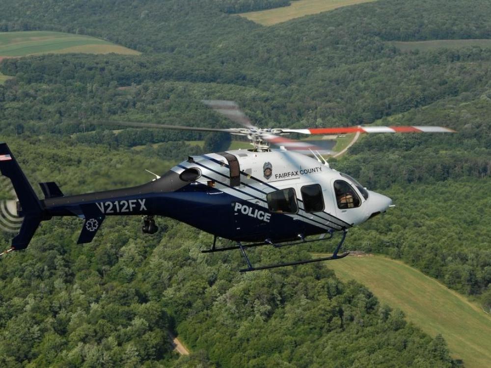 Side view of white and black helicopter in flight with four-blade propellor. The word "Police" is painted in white in the center of the fuselage.