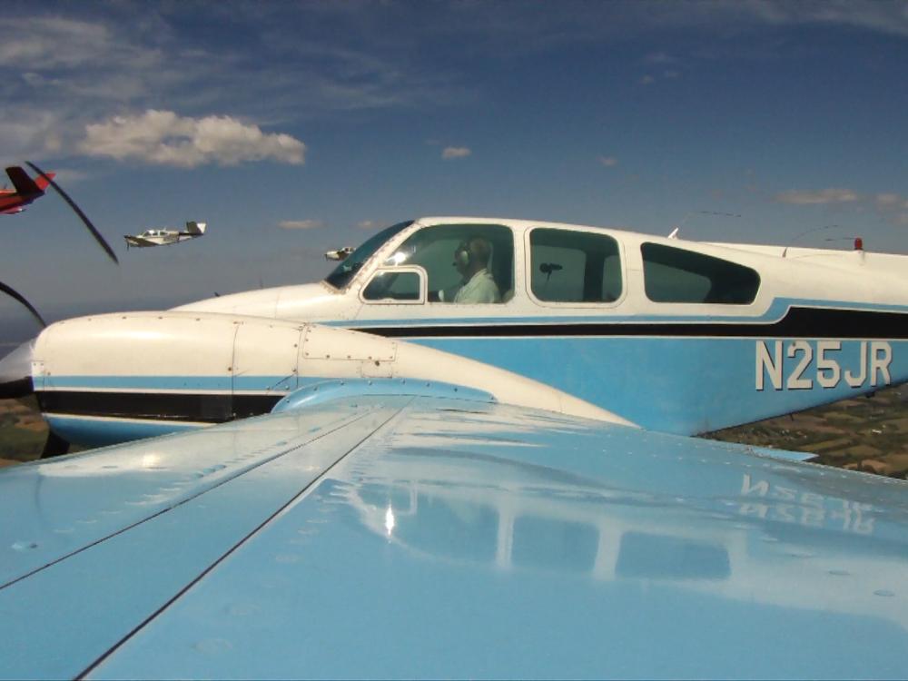 Side view of white and light blue monoplane in flight with twin engines. Registration number "N25JR" is painted in white near the rear of the fuselage.