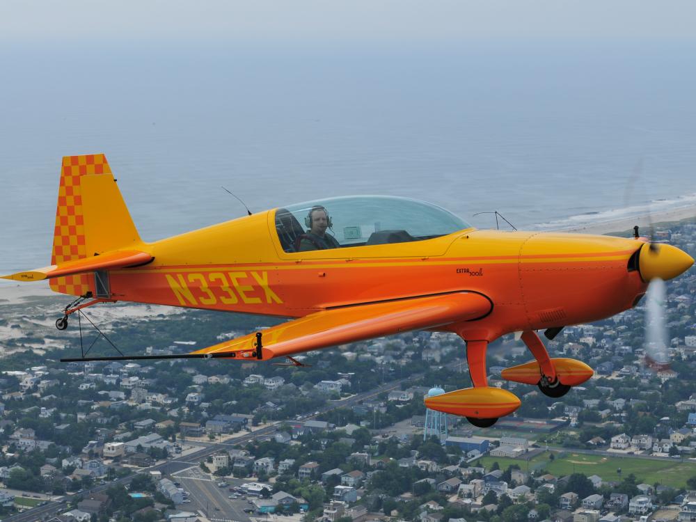 Side view of yellow and orange monoplane with single engine and fixed landing gear. Registration number "N33EX" is painted in yellow behind the cockpit.