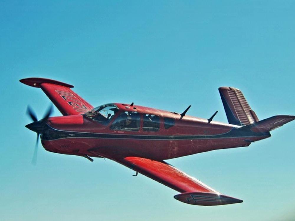 Side view of red and black monoplane in flight with single engine.