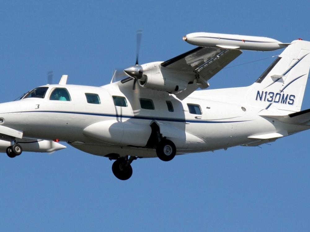 Side view of white monoplane in flight with twin engines. Registration number "N130MS" is painted in blue on the vertical stabilizer.