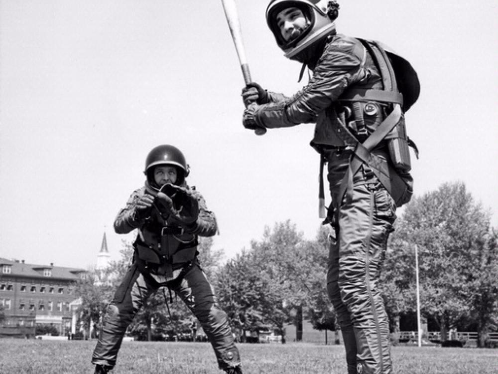 Two people play baseball in suits intended for use in space.