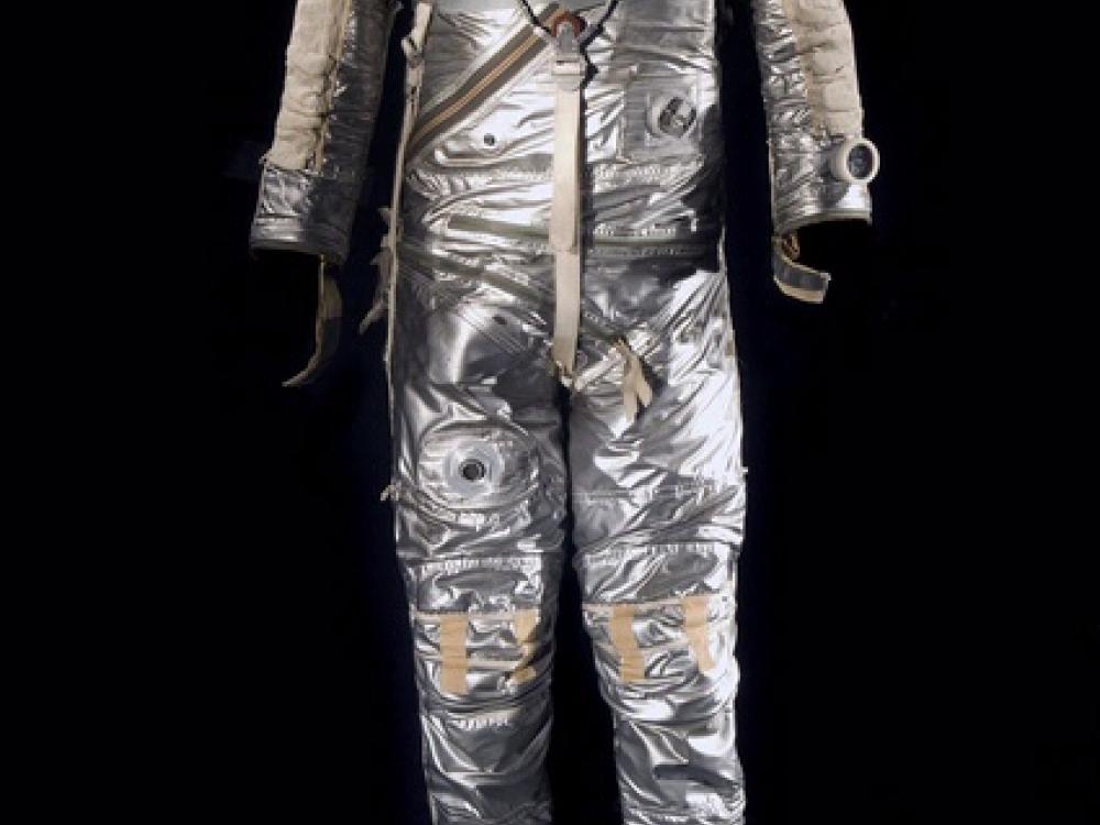 Silver-colored spacesuit with multiple tubes used for life support as well as openings for a helmet and gloves.