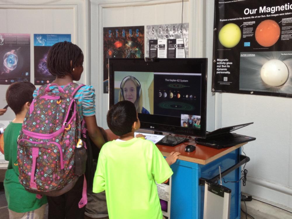 Three museum visitors speak with a museum expert who chats with them through video chat on a computer.