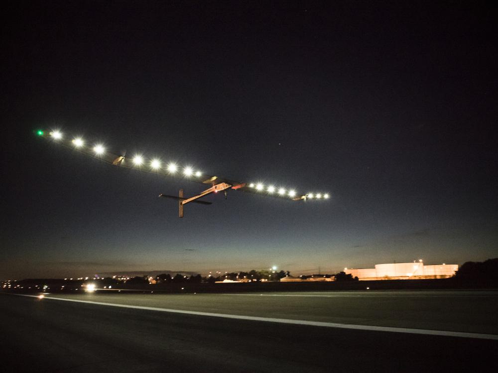 A plane with very long wings lined by lights departs an airport.