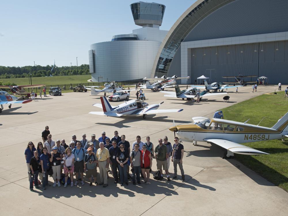 A group of individuals stand on a runway with several planes parked behind them.