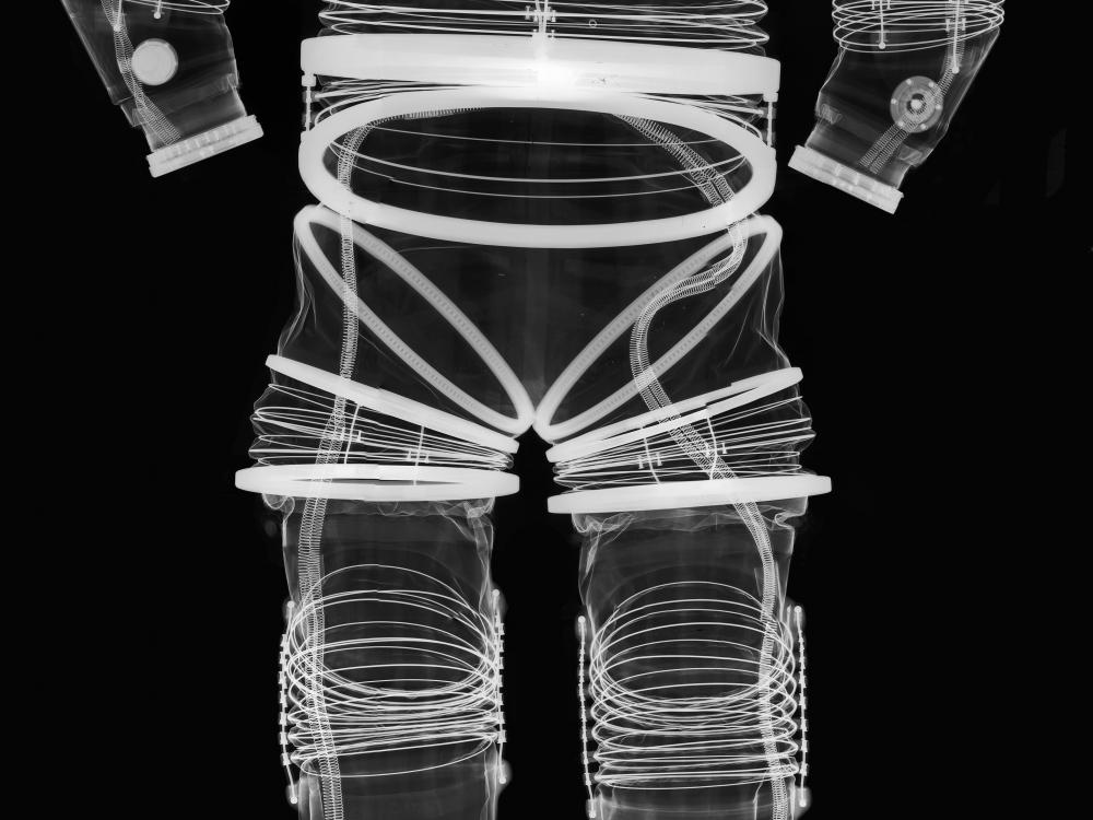 Negative x-ray of the front view of an early, experimental full-body spacesuit. Full flexibility can be seen in joint regions through the spring-like appearance of white lines around joints.