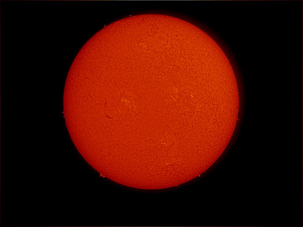 Disk view of the Sun's atmosphere with one prominence of floating gas on the bottom left edge of the Sun and a filament of floating gas visible in the middle left side of the disk. A few phages of lighter colors are also visible across the image.