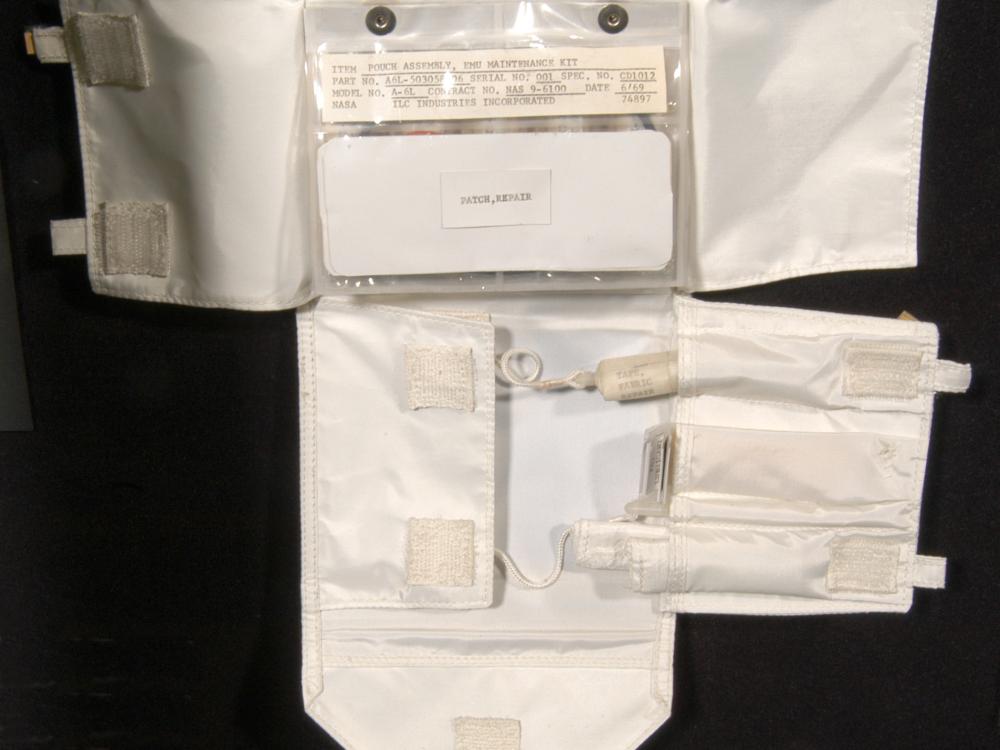 Small maintenance kit made with white fabric and velcro to keep items in place. Multiple items inside small plastic-like bag on upper layer, with three tools visble in a lower section.