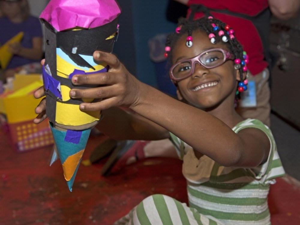 A young girl displays her colorful, finished art project during a family event at the museum.