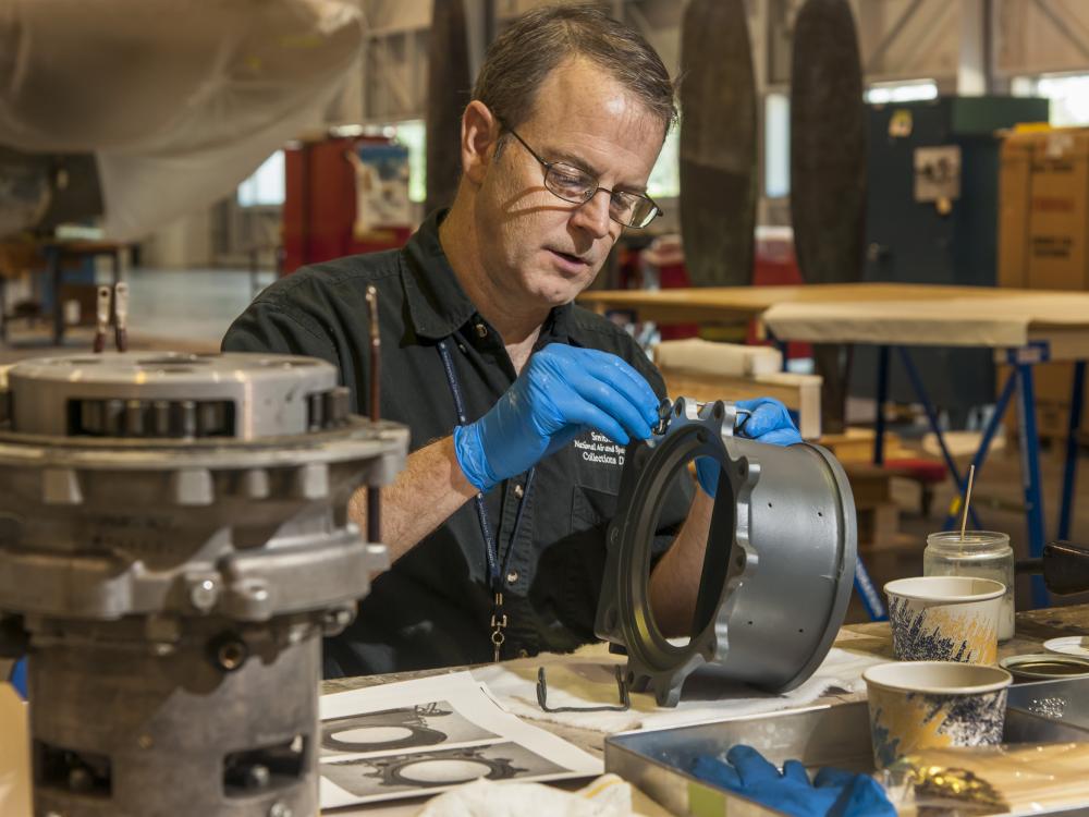 A male staff member of the museum's Collections Department works on restoring part of a World War II era bomber in the museum's restoration hangar.