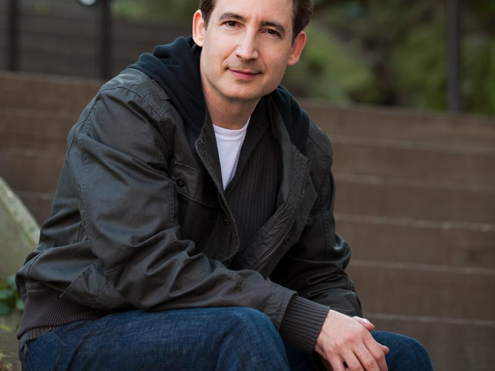 Dr. Brian Greene, a white man, sits as he poses for a portrait.