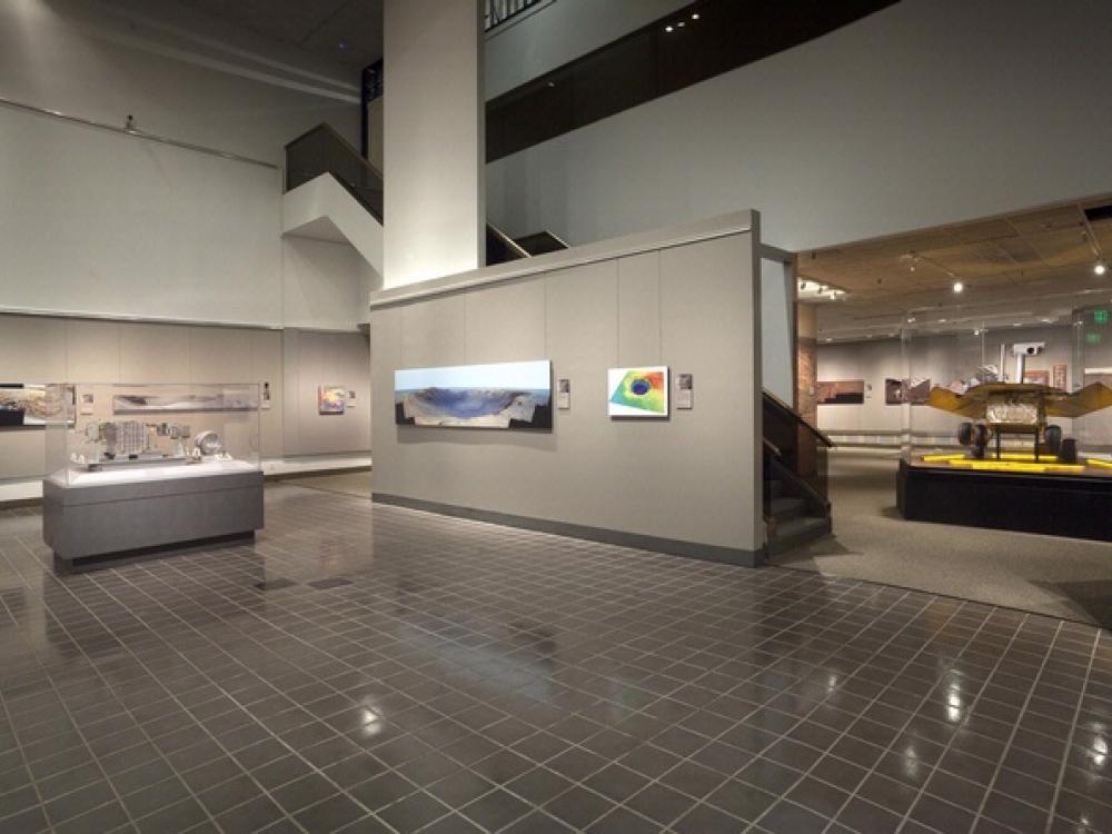 An open area of an exhibit on Mars Rovers with nearby pictures of Mars taken by the Rovers and a small exhibit table.