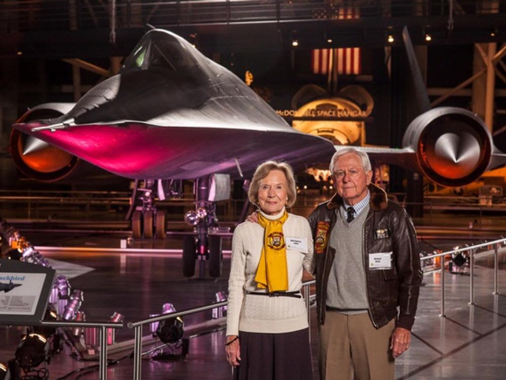 Richard and Anne Jones, a couple consisting of a white man and woman, pose together in front of the Blackbird on display in the Museum.