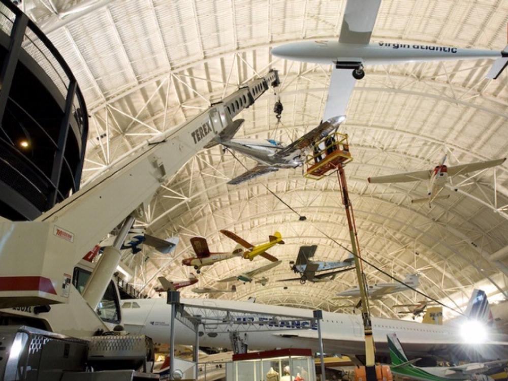 Museum staff members hang a silver monoplane onto the roof of the aircraft hangar at the Steven F. Udvar-Hazy Center.