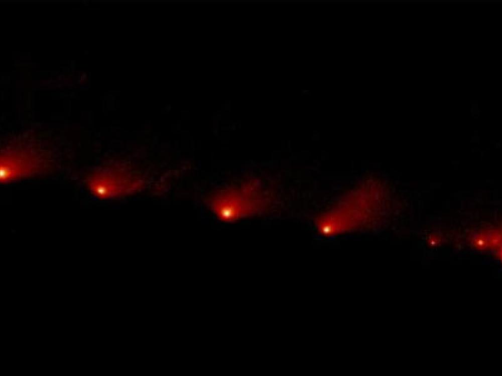 A view of a comet as it soars across space, leaving a red trail of dust behind a lighter red dot.