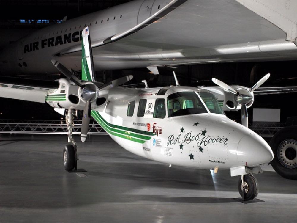 Partial side view of white monoplane with black and green stripes lining the side of the plane. The monoplane has two twin engines, one on each wing.