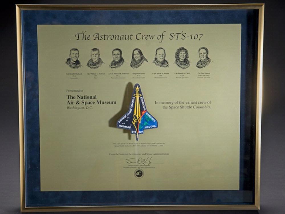 A plaque honoring the members onboard the Space Shuttle Columbia during the STS-107 disaster with their faces and a depiction of the shuttle engraved into the plaque.