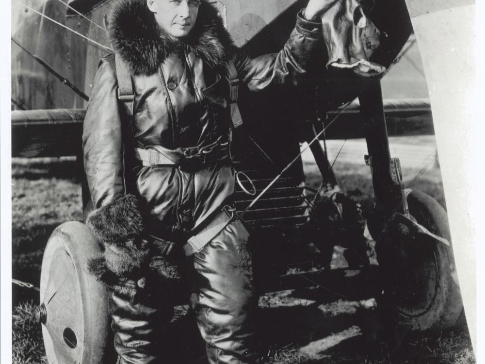 Lt. John Macready, a white man, stands in aviator gear next to an aircraft.