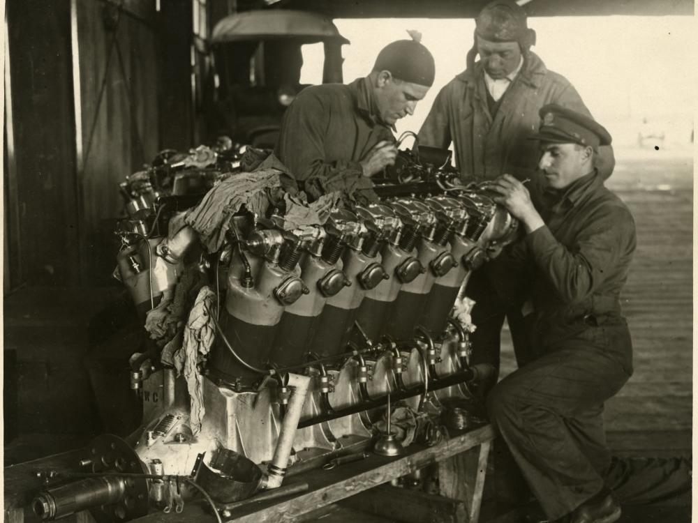 Three people examine a twelve-cylinder engine used for long-travel flight.