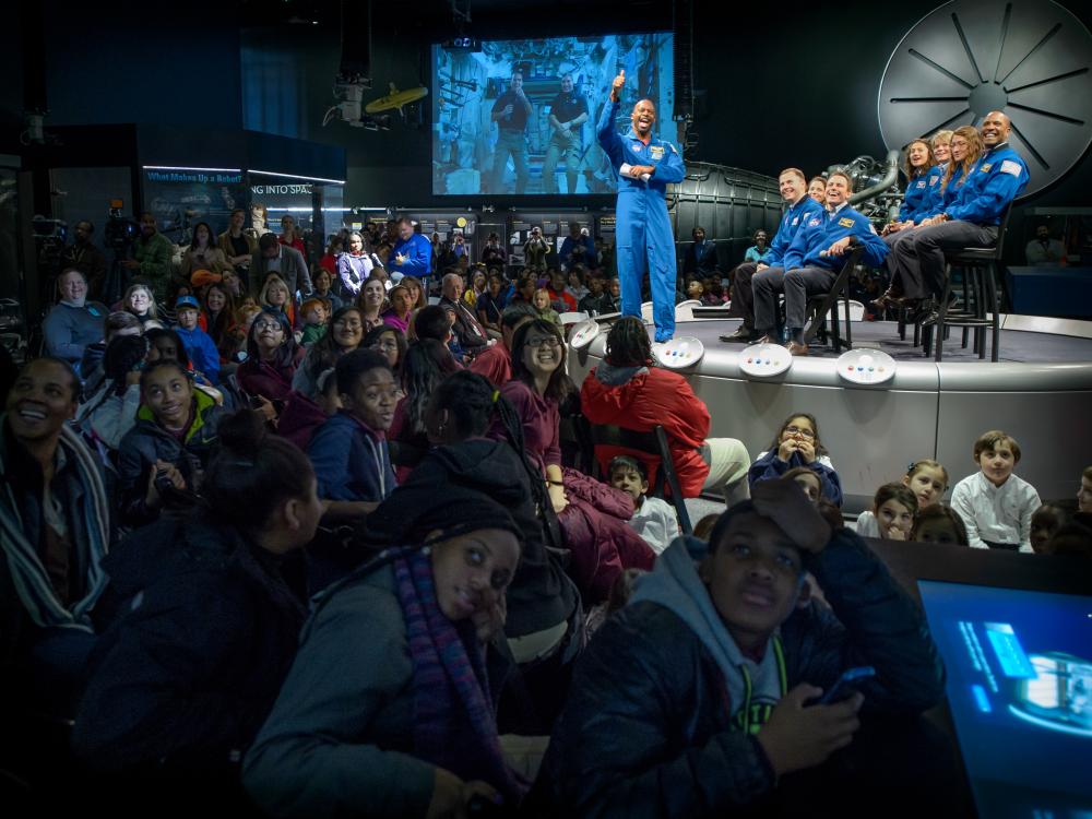 A former astronaut gives a thumbs up gesture to a camera streaming a video chat with astronauts on the International Space Station.