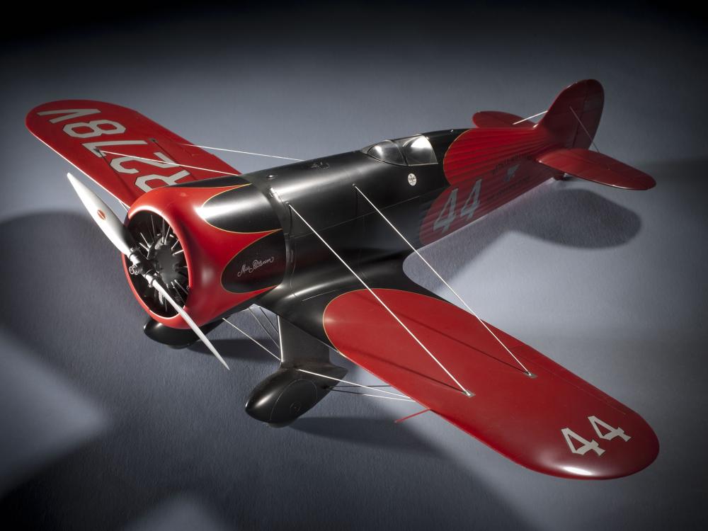 Model of a red and silver-colored monoplane with one engine. Number 44 is painted on the left wing and behind the cockpit of the plane.