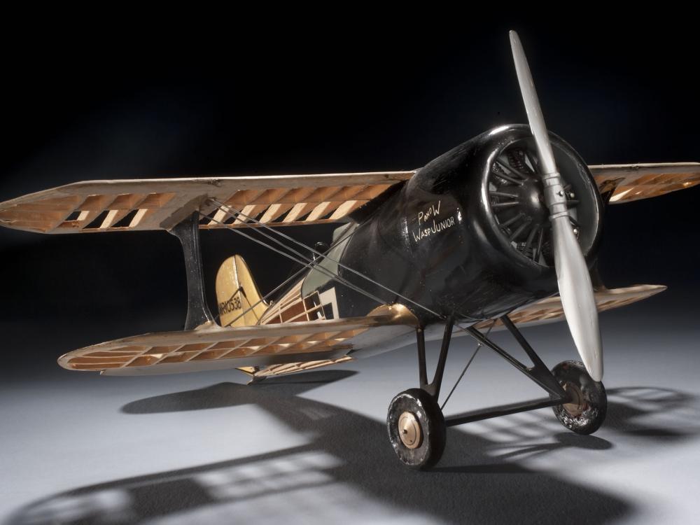 Front-facing view of wooden and black-colored metal biplane model with one engine.