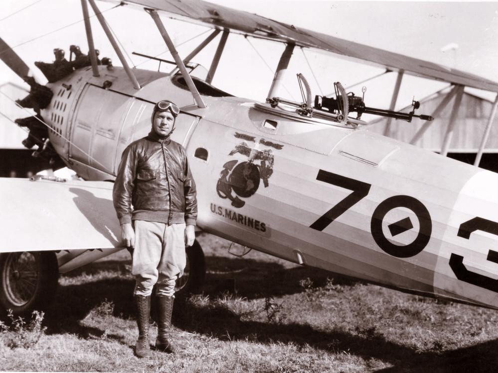 C. Frank Schilt, a white male pilot, stands next to an aircraft wearing aviator gear.