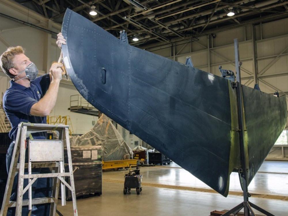 A male museum specialist prepares the tail section of a blue military monoplane for painting.