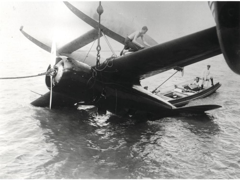 Charles Lindbergh stands atop an capsized aircraft, inspecting it for damage.