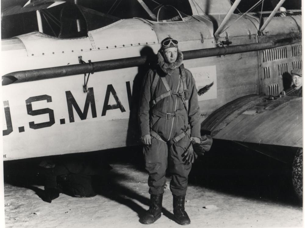 Charles Lindbergh stands in front of an aircraft wearing aviator gear.