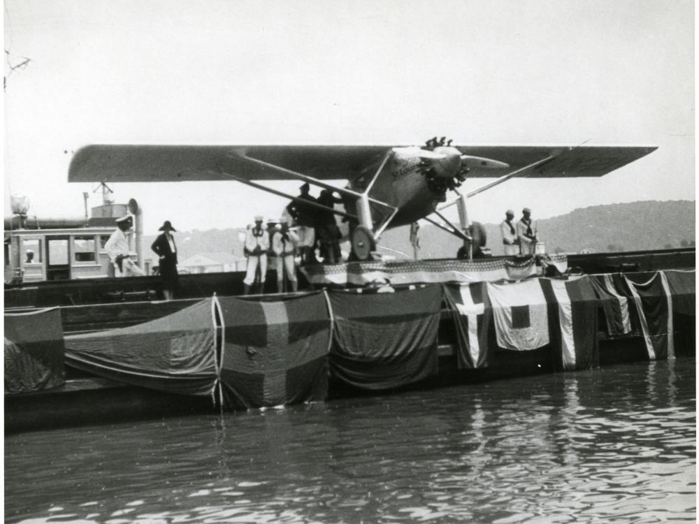 The Spirit of St. Louis sits on a barge as it is exhibited following Charles Lindbergh's record-breaking transcontinental flight. Flags are hung across the side of the barge.