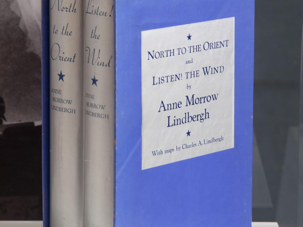 A blue bookcase featuring two books with silver-colored spines written by Anne Morrow Lindburgh about her flights with Charles Lindbergh.