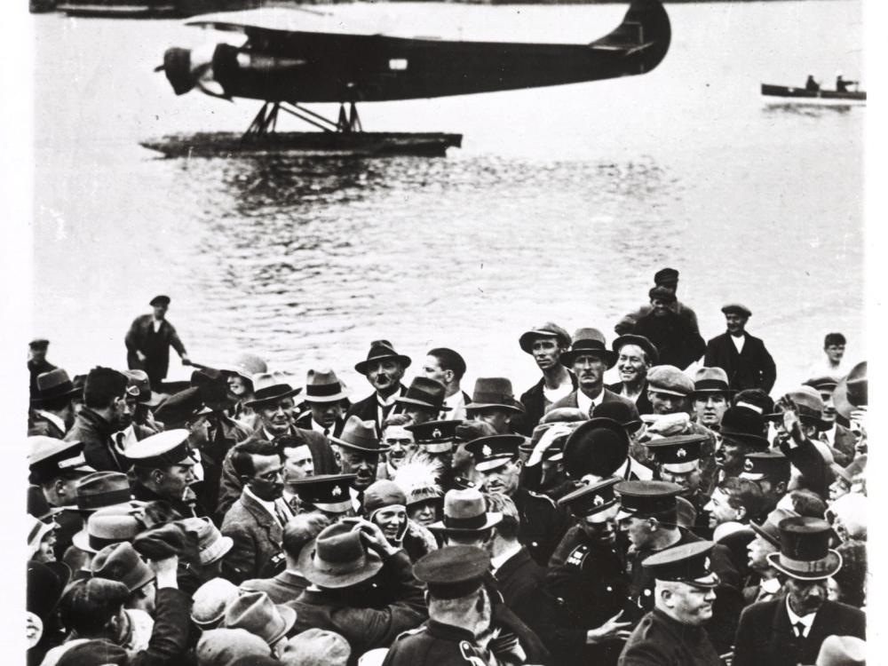 People flock to see a monoplane with pontoon floats that is stationary in a body of water.