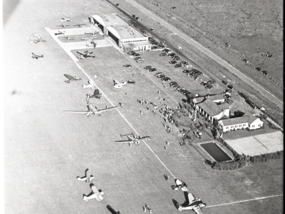 View of an aviation-focused country club from an aircraft. Planes are scattered near two buildings next to a road.